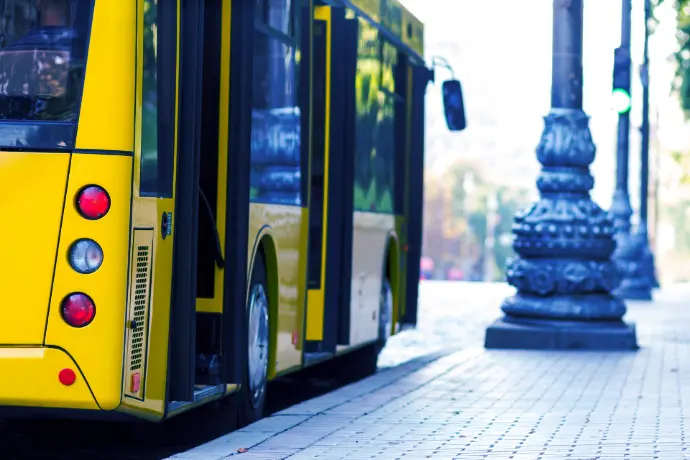 Devices for real-time navigation and ticketing in public transport Close-up of yellow city bus at station with blurred passengers in background