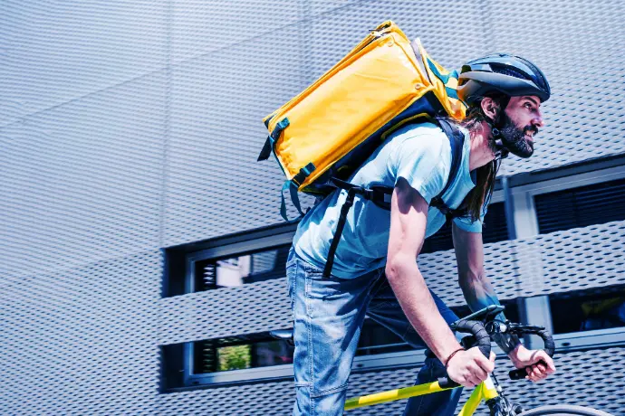 Tablets and handhelds for bike and scooter couriers Delivery rider on bicycle carrying a yellow backpack in an urban environment